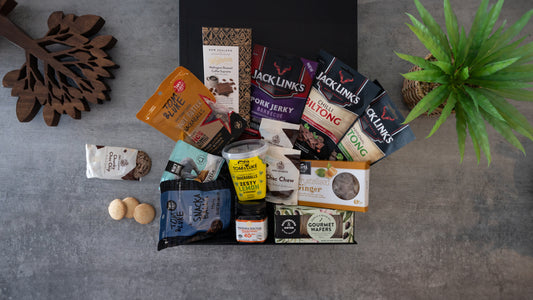 Assorted snacks and treats on a gray surface with a plant in the background. #Gift#SwaggerBox#Archies#GiftBox